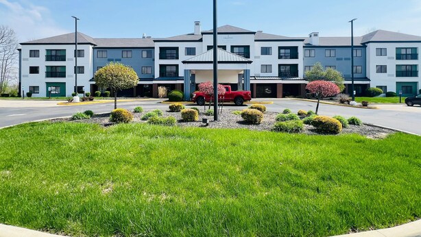 A multi-story hotel with a central courtyard, a red truck parked in the driveway, and well-maintained landscaping.