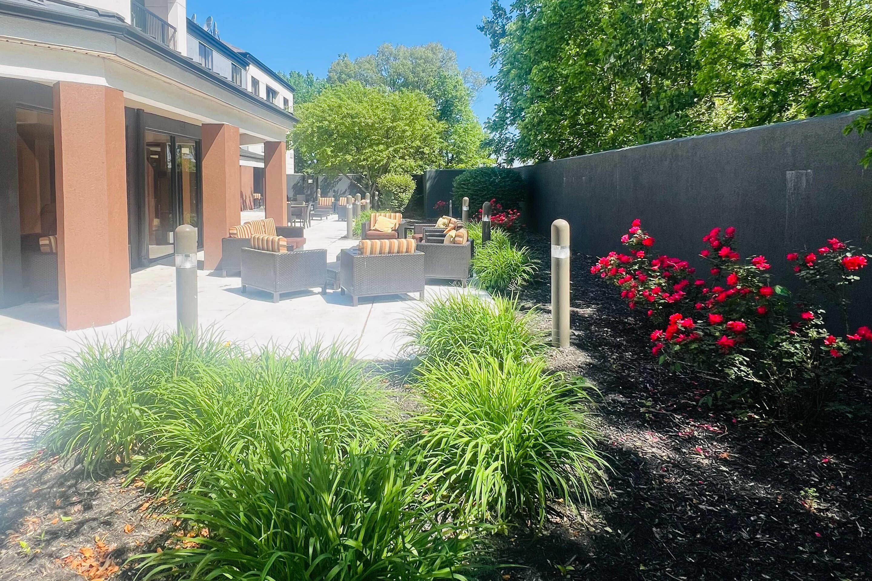 Un patio con mobiliario exterior, un jardín con flores rojas y un edificio de diseño moderno.