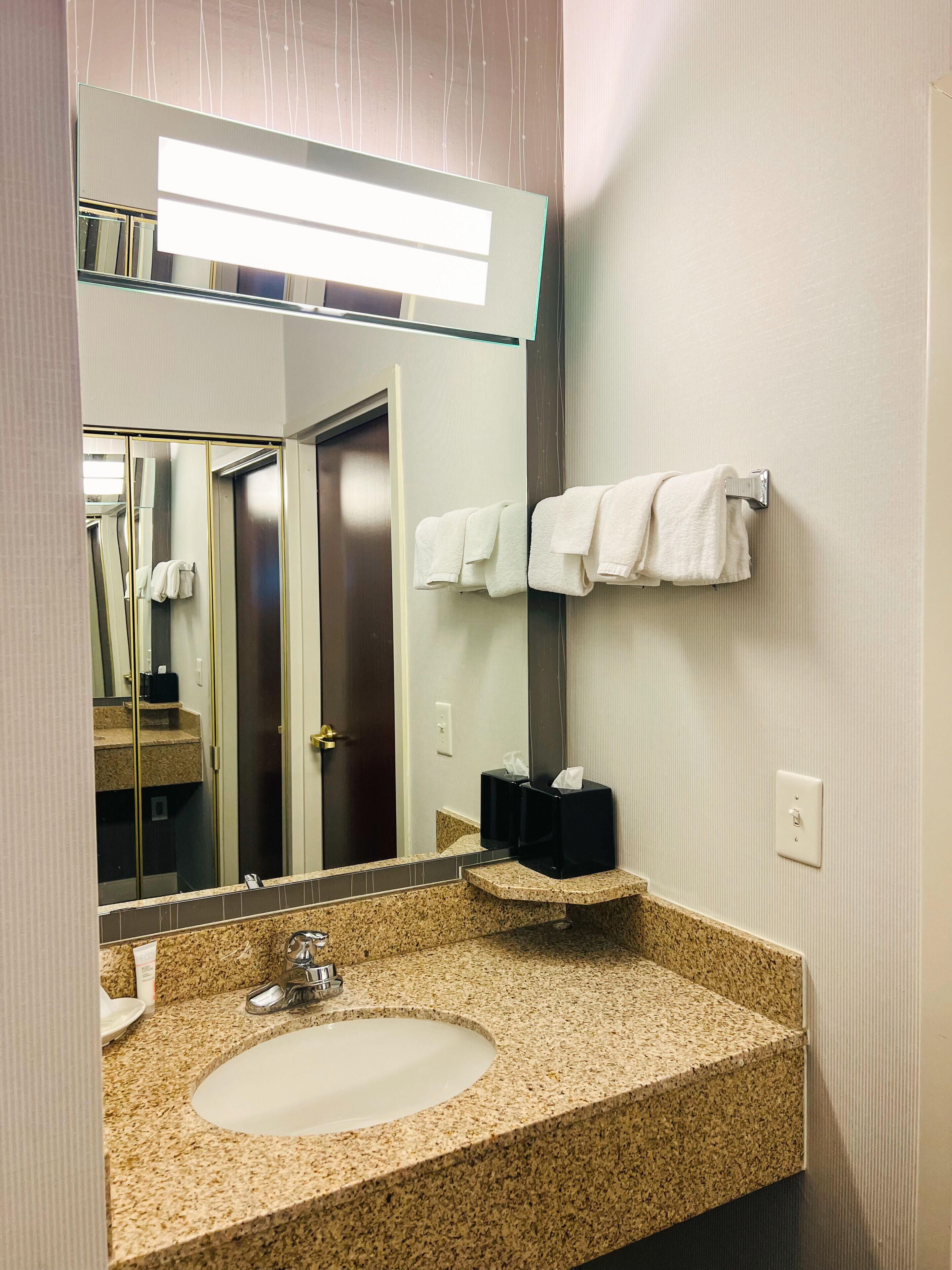 A bathroom with a granite countertop sink, a large mirror, and a towel rack with folded towels.