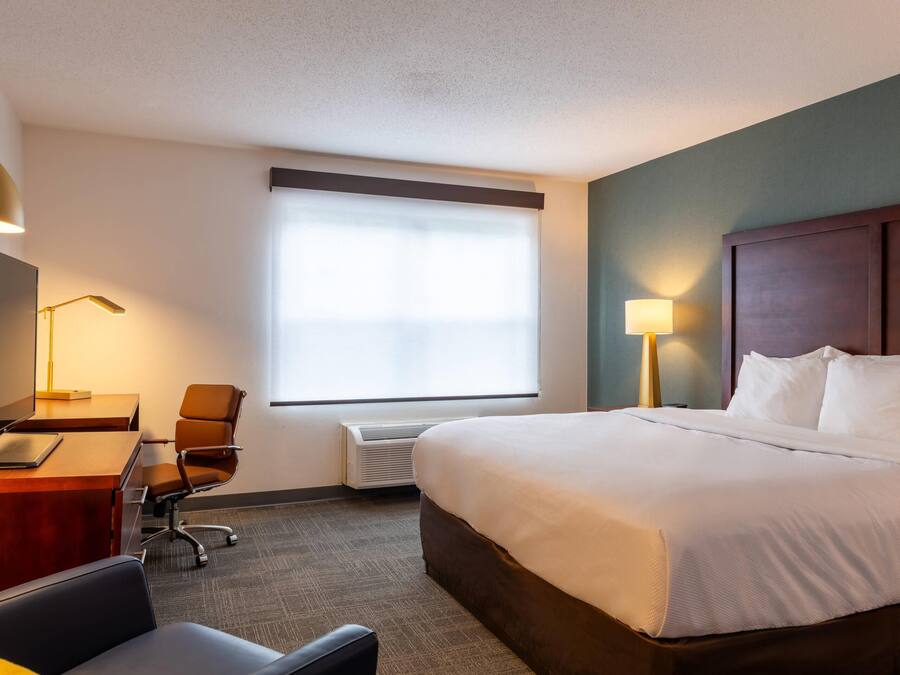 Habitación de hotel con cama, escritorio, silla y un ventanal con persianas.