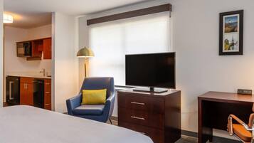 Habitación de hotel con cama, escritorio con televisor, silla, lámpara y un cuadro en la pared.