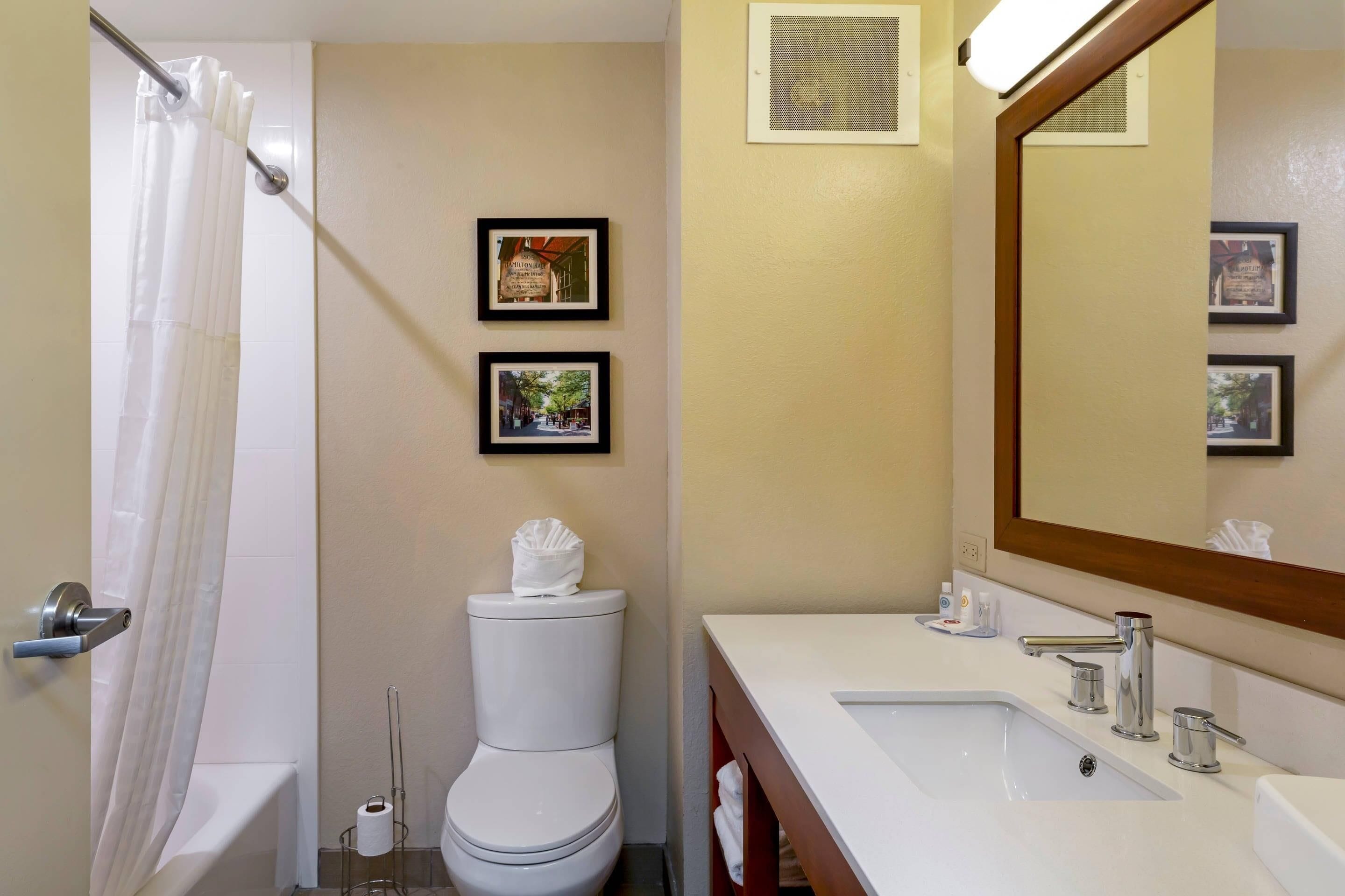A bathroom with a shower, toilet, sink, and framed pictures on the wall.