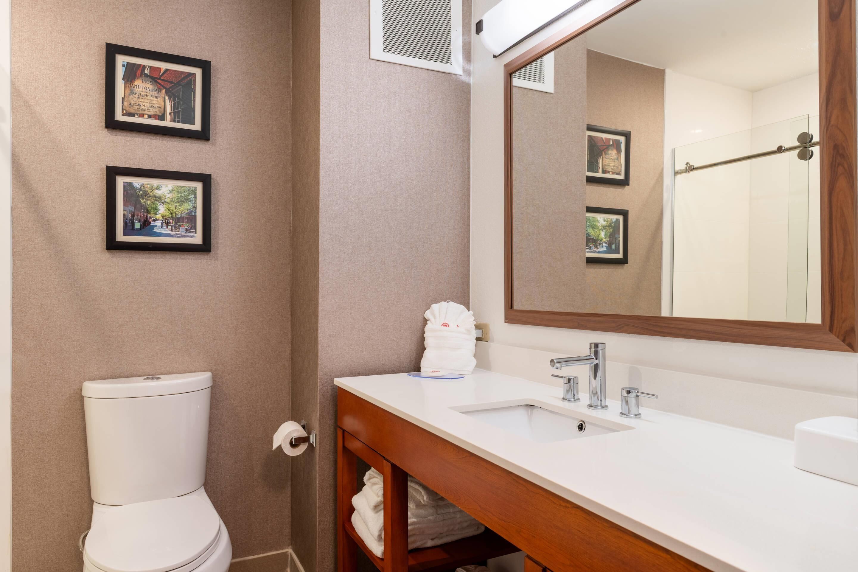 A bathroom with a toilet, sink, mirror, and framed pictures on the wall.