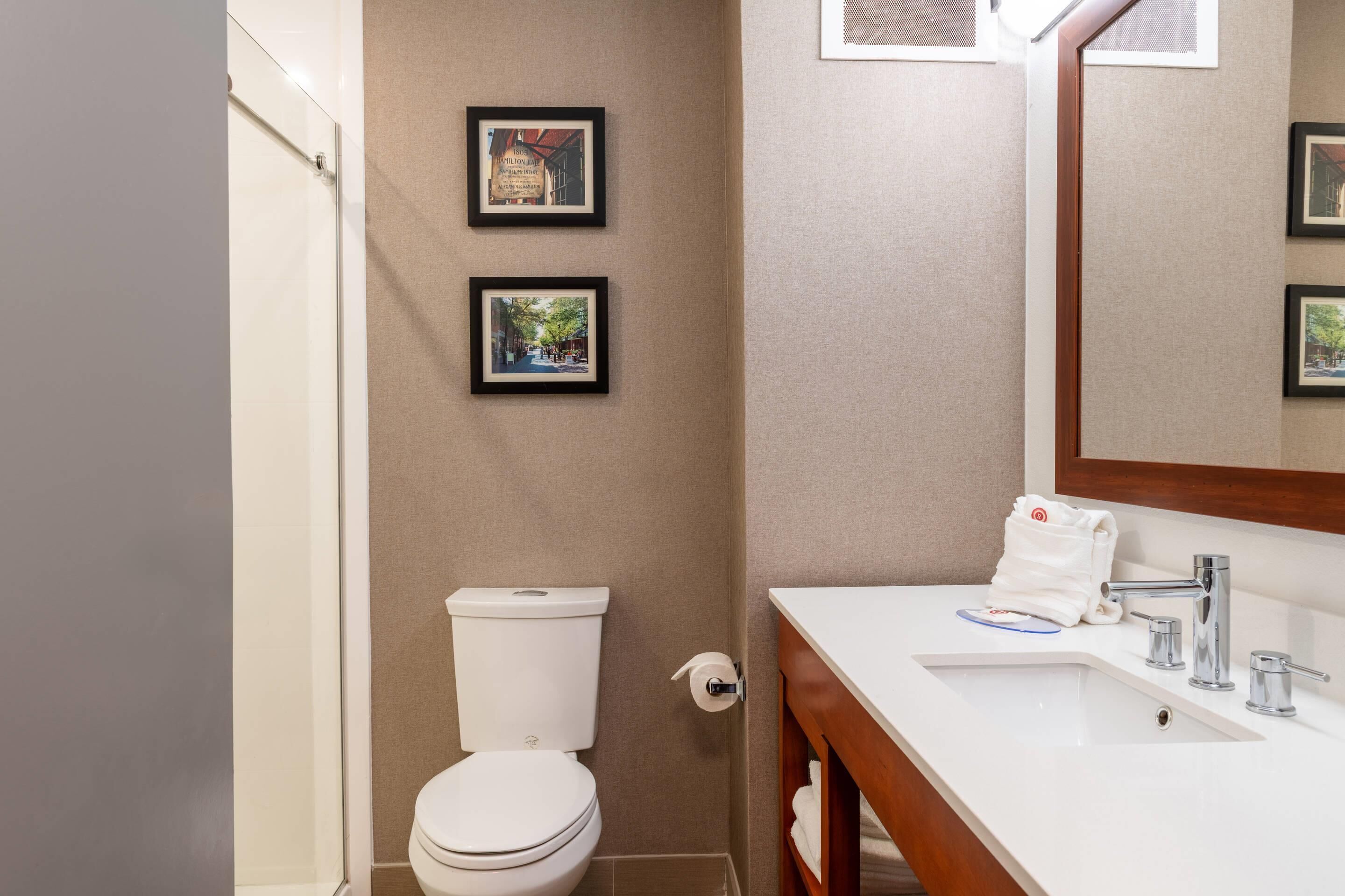 Un baño con inodoro blanco, lavamanos con espejo y dos cuadros en la pared.