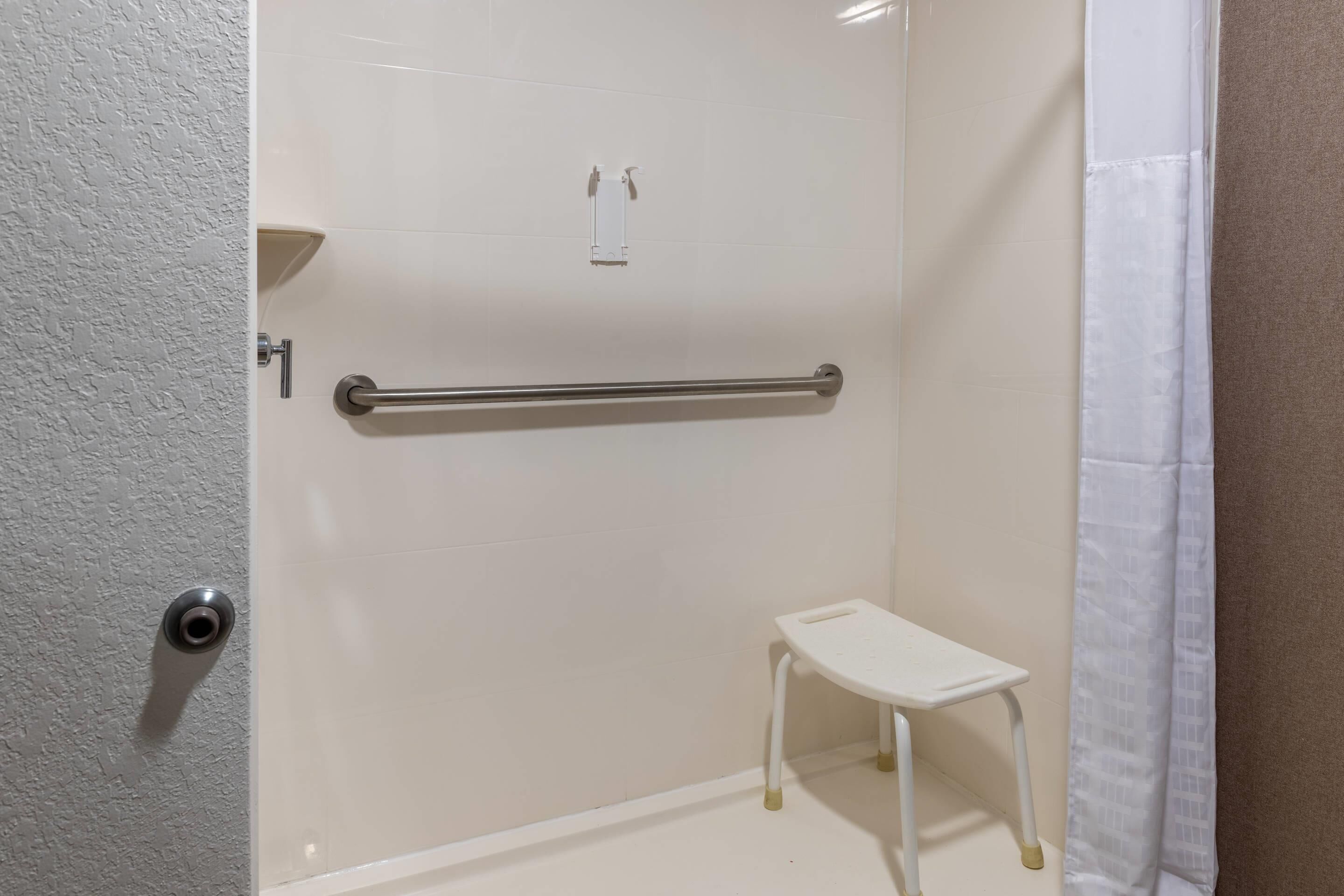 A bathroom with a white tiled wall, a grab bar, a small white bench, and a shower curtain.