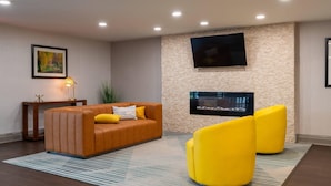 Una sala de estar moderna con un sofá de cuero marrón, sillones amarillos, un televisor de pantalla plana montado en una pared de piedra y una mesita con una lámpara.