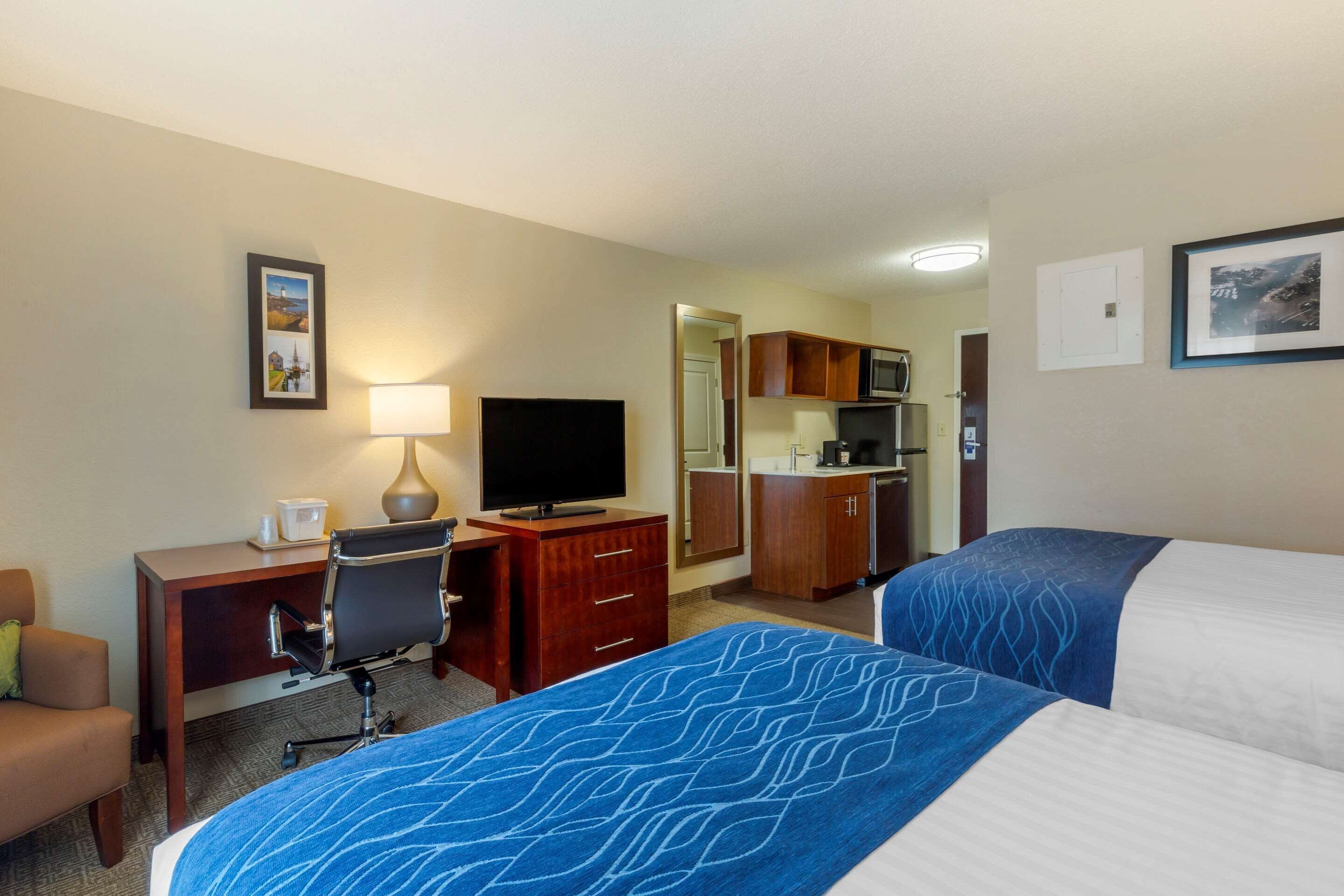 A hotel room with a bed, desk, chair, television, and kitchenette.