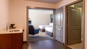 Habitación de hotel con un armario de madera, un lavabo, una silla y una cama con colchón y almohadas.