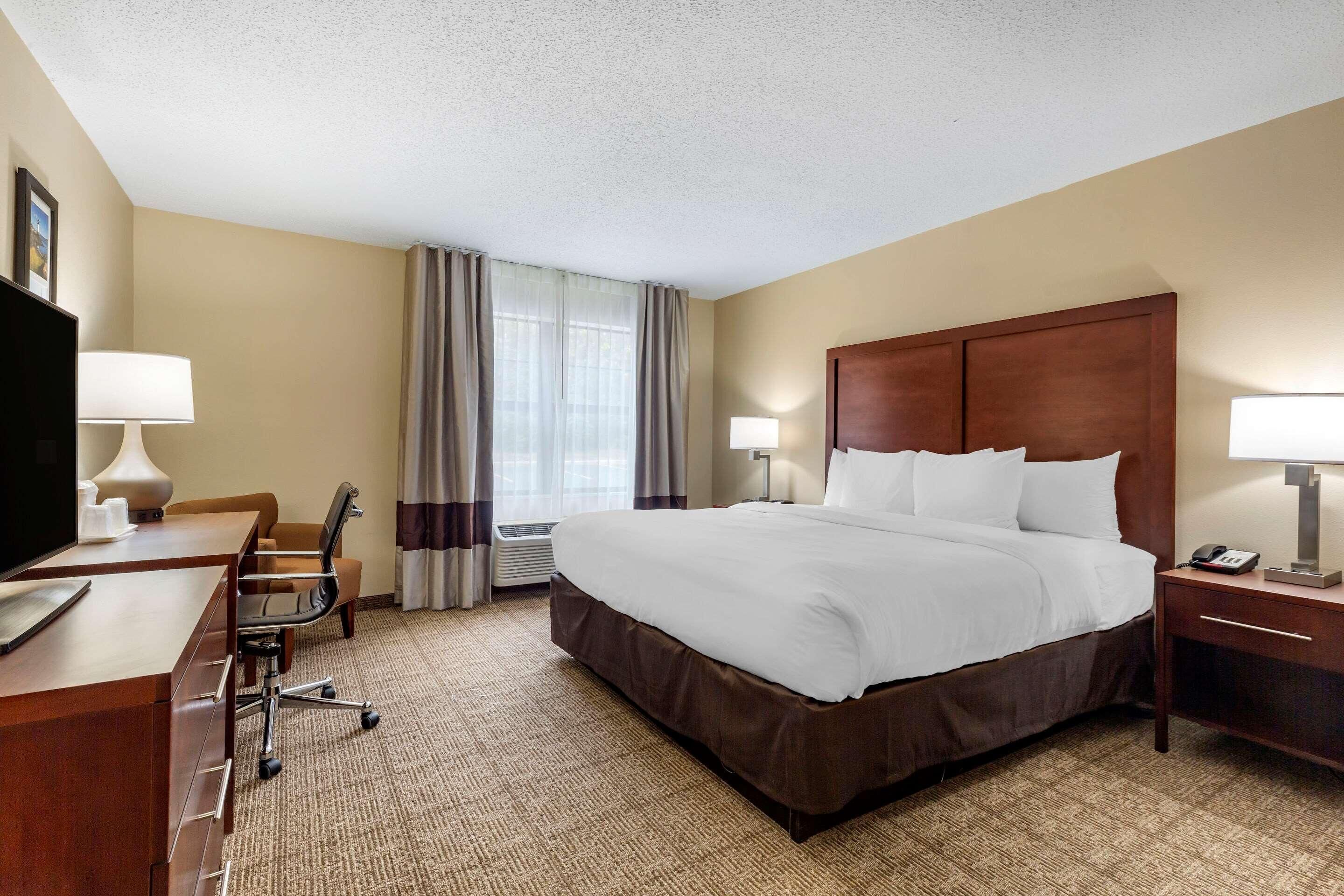 Une chambre d’hôtel avec un grand lit, un bureau avec une chaise, une télévision et une table de chevet avec une lampe.