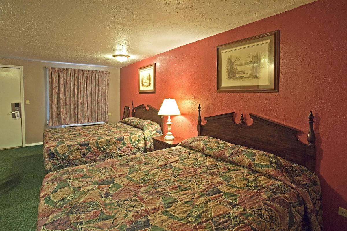 A hotel room with two beds, a lamp, and a painting on the wall.