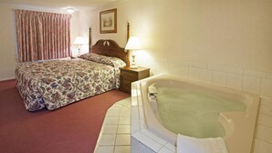 A hotel room with a large bed, a separate bathroom with a bathtub, and a nightstand with lamps. - Americas Best Value Inn Lansing (Lansing)