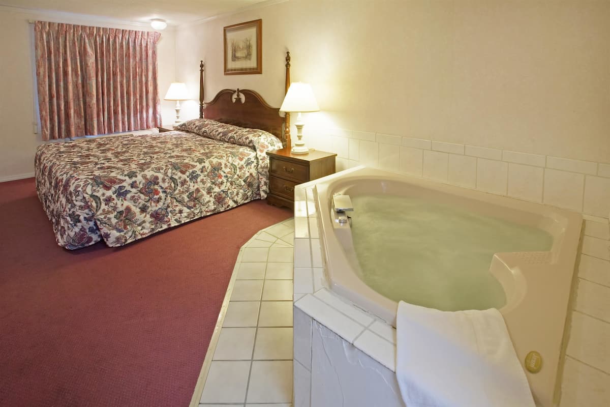 A hotel room with a large bed, a separate bathroom with a bathtub, and a nightstand with lamps.