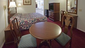 A hotel room with a bed, a desk with a chair, a round table, a dresser, a television, and a mirror. - Americas Best Value Inn Lansing (Lansing)