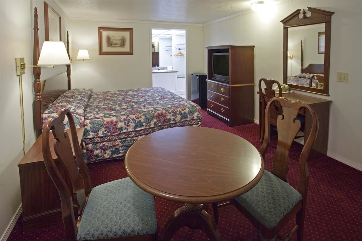 A hotel room with a bed, a desk with a chair, a round table, a dresser, a television, and a mirror.