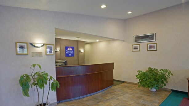 A reception area with a wooden reception desk, a potted plant, and a sign indicating the hotel is a Best Value Inn. - Americas Best Value Inn Lansing (Lansing)