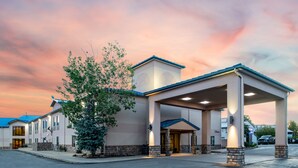 A hotel with a covered entrance, stone pillars, and a large tree in front.