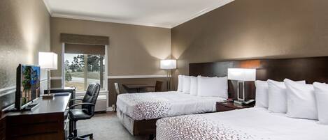 Ett hotellrum med två sängar, ett skrivbord, en stol och ett fönster med utsikt över träd.