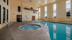 An indoor swimming pool with a hot tub, lounge chairs, and a door leading to another room.
