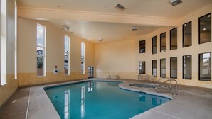 An indoor swimming pool with clear water, surrounded by beige walls and large windows.