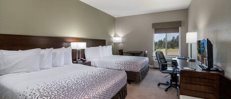 Une chambre d’hôtel avec deux lits, un bureau avec un ordinateur, une chaise et une fenêtre donnant sur des arbres.