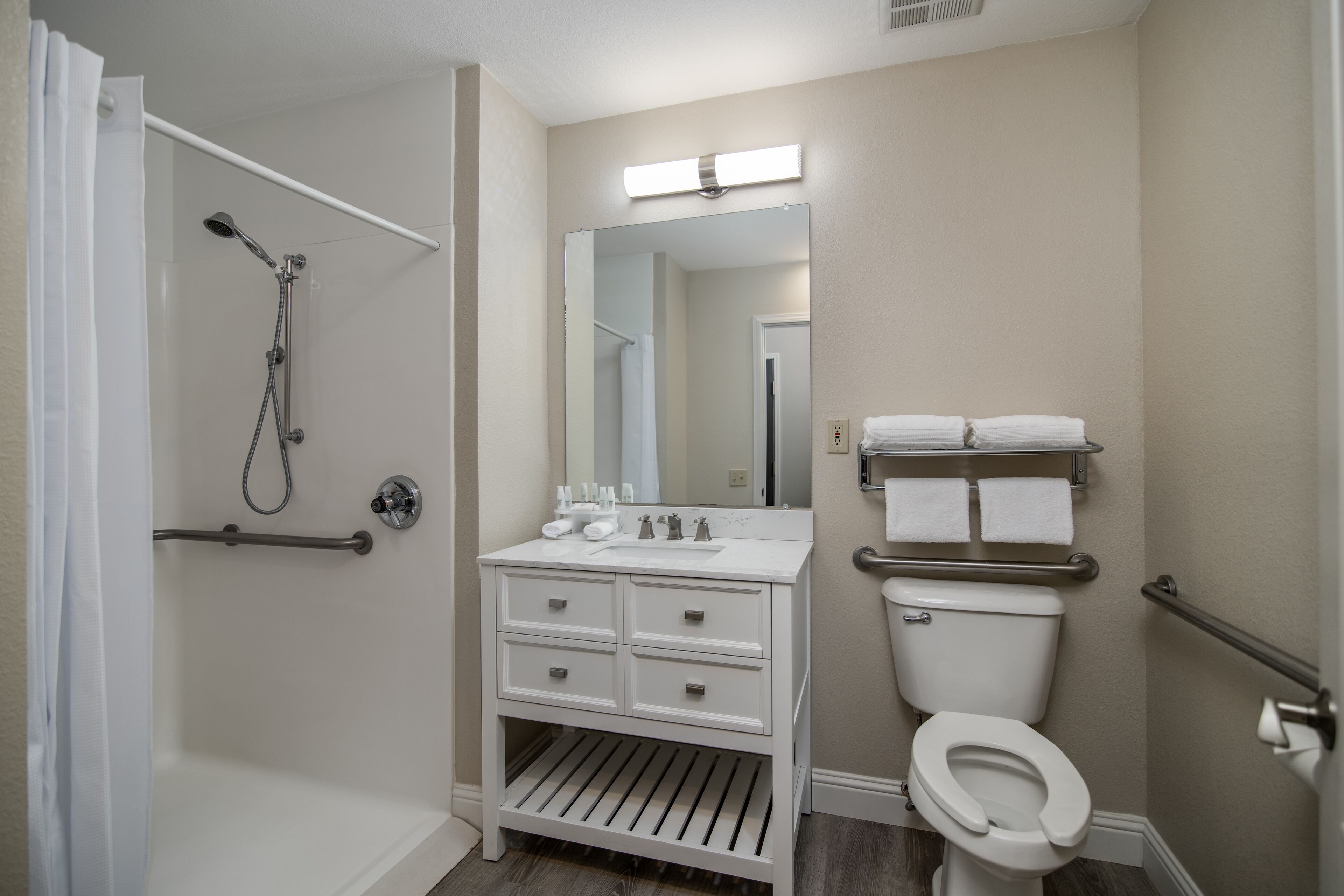 A bathroom with a shower, toilet, vanity, and a mirror.