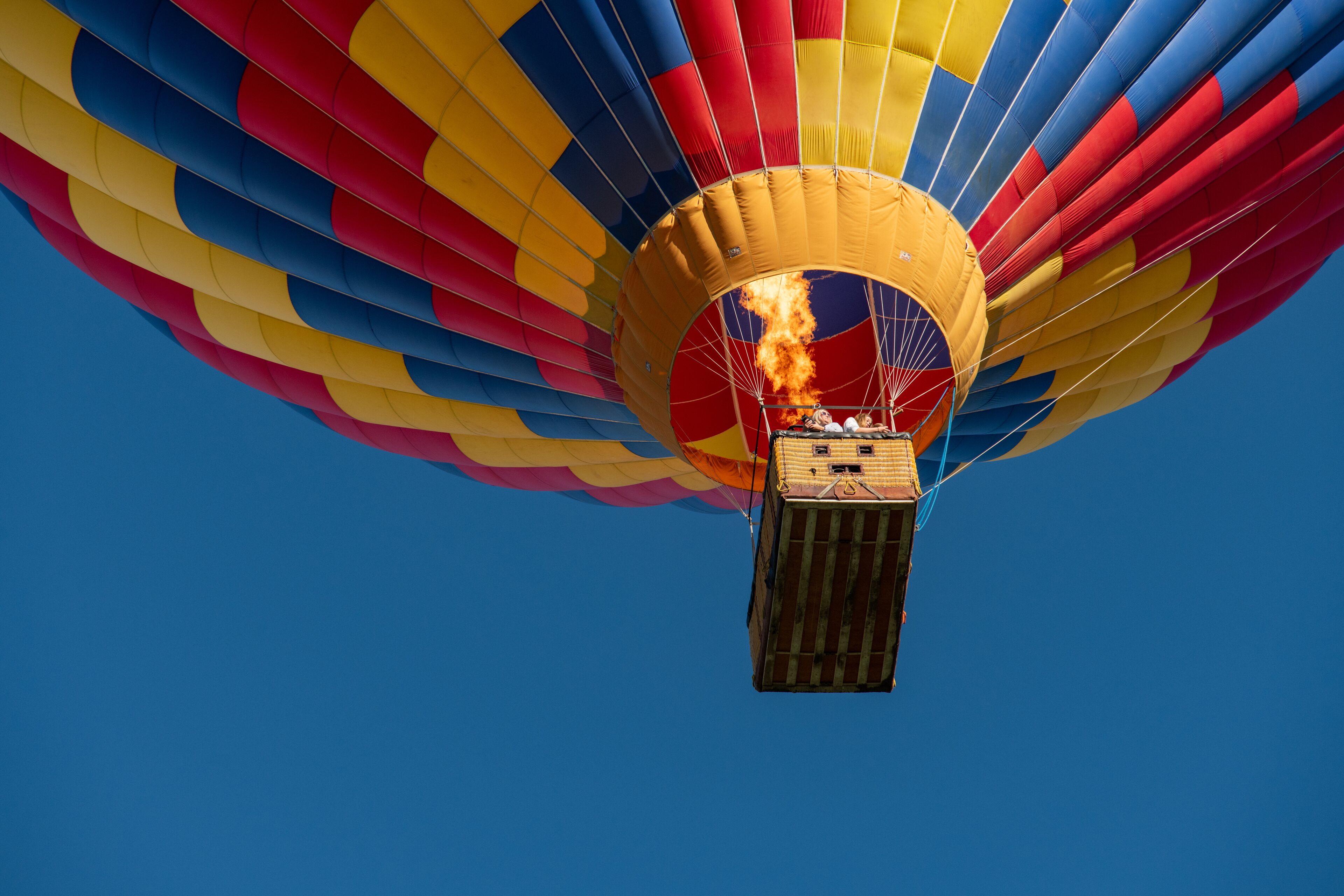 En varmluftsballon med en kurv af træ og ild inde i kurven, mod en klar blå himmel.