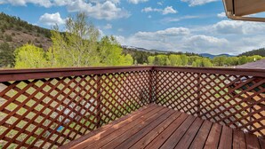 Una terraza de madera con barandilla enrejada que da a un paisaje montañoso con árboles y cielo despejado.