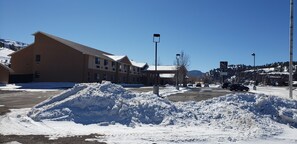 Ein Gebäude mit flachem Dach und mehreren Fenstern, ein mit Schnee bedeckter Parkplatz und ein klarer, blauer Himmel.