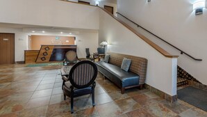 Un amplio vestíbulo con una escalera, un mostrador de recepción, un sofá y una silla.