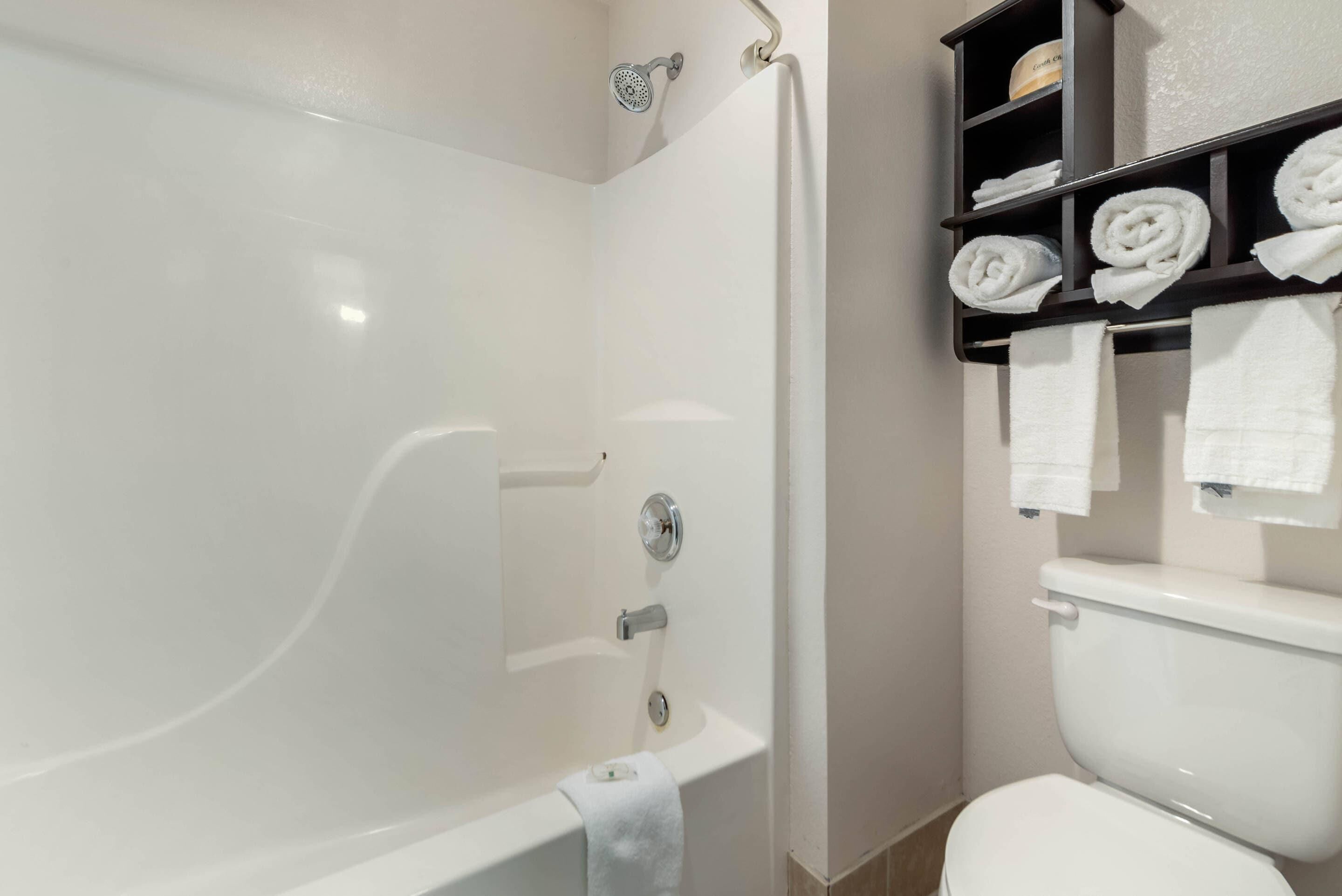 A bathroom with a bathtub, toilet, and shelves with towels.