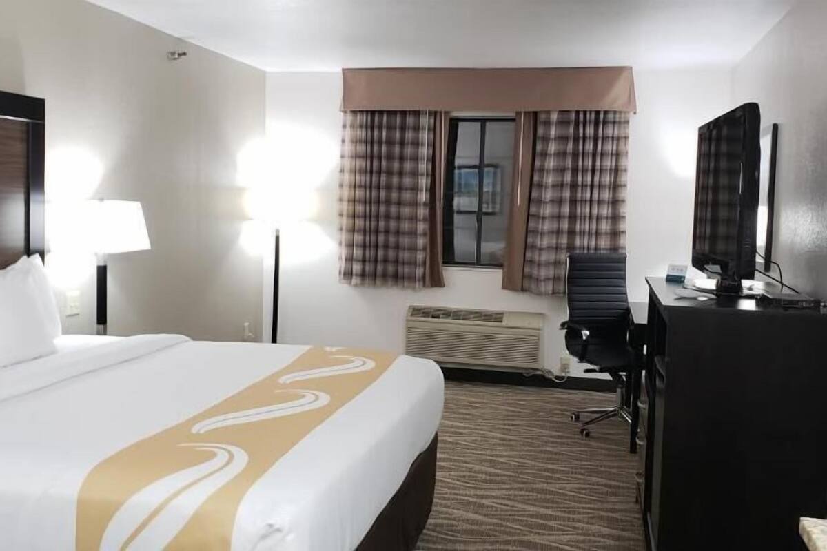 A hotel room with a bed, a desk, a chair, a television, and a window with curtains.