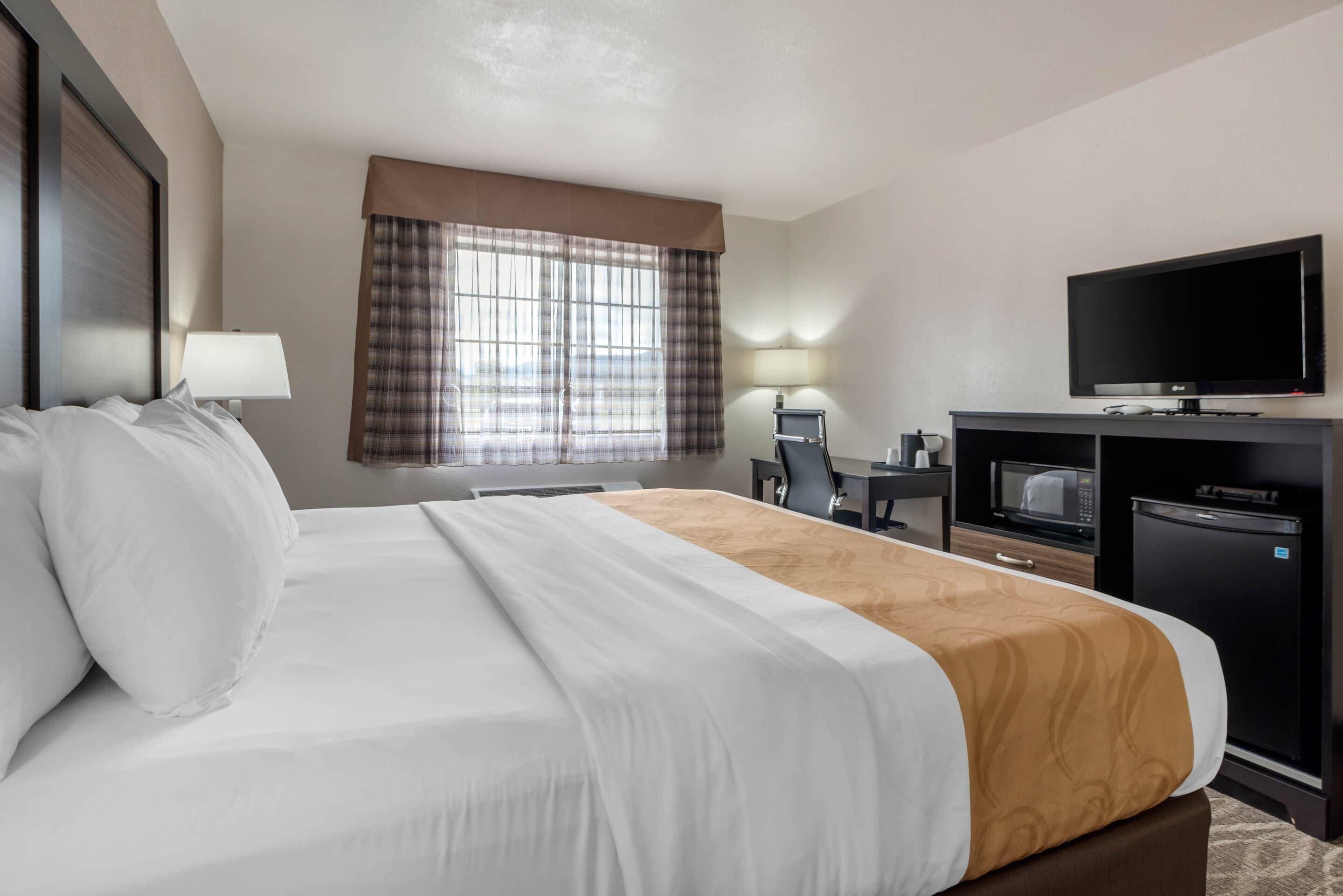 A hotel room with a large bed, a desk with a computer, a TV, and a microwave.