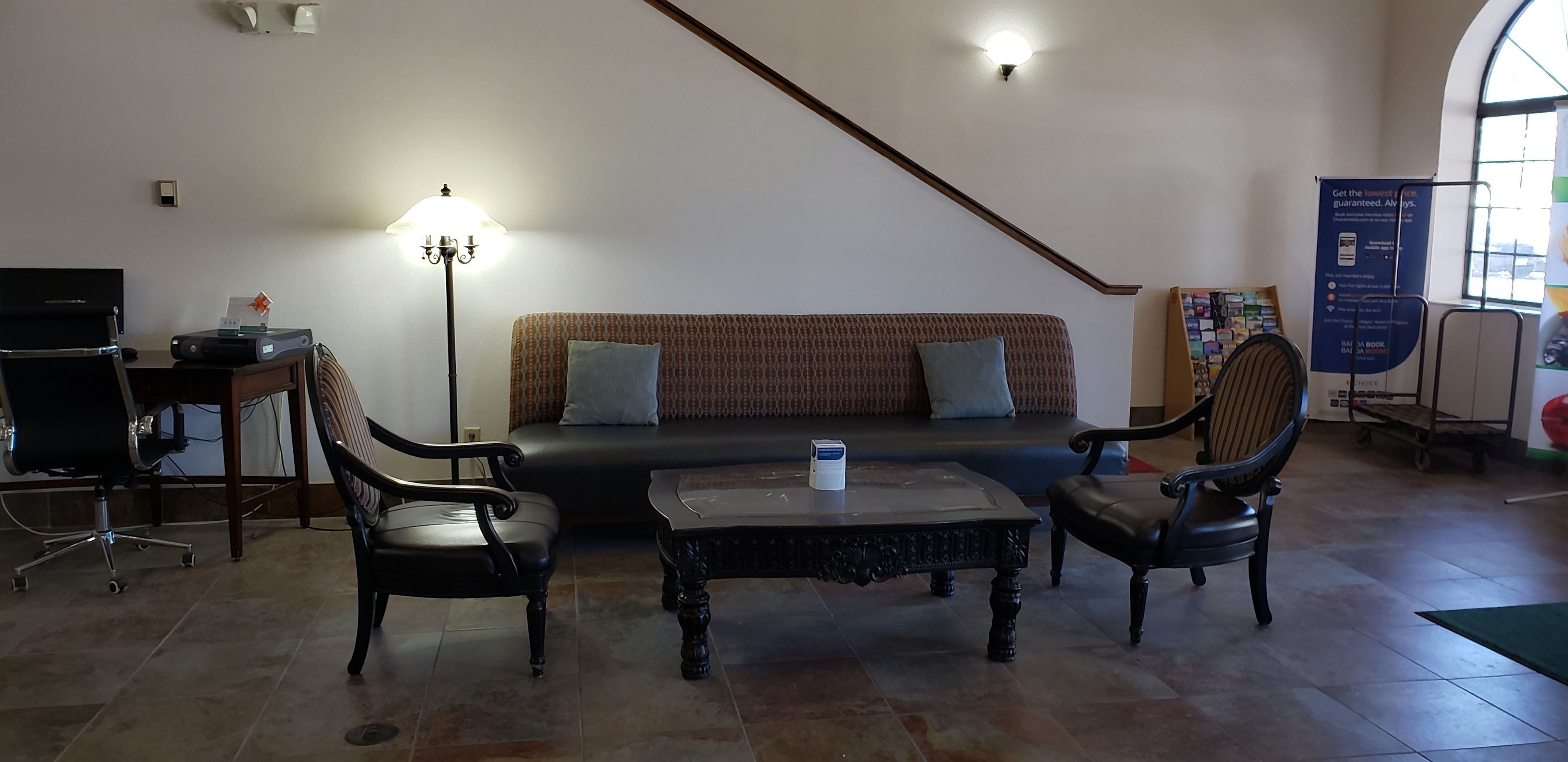A room with a sofa, two armchairs, a coffee table, a lamp, a desk with a computer, and a poster on the wall.