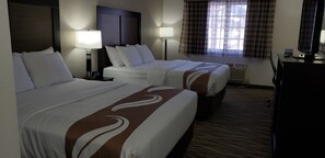 A hotel room with two beds, a desk, and a window with curtains.