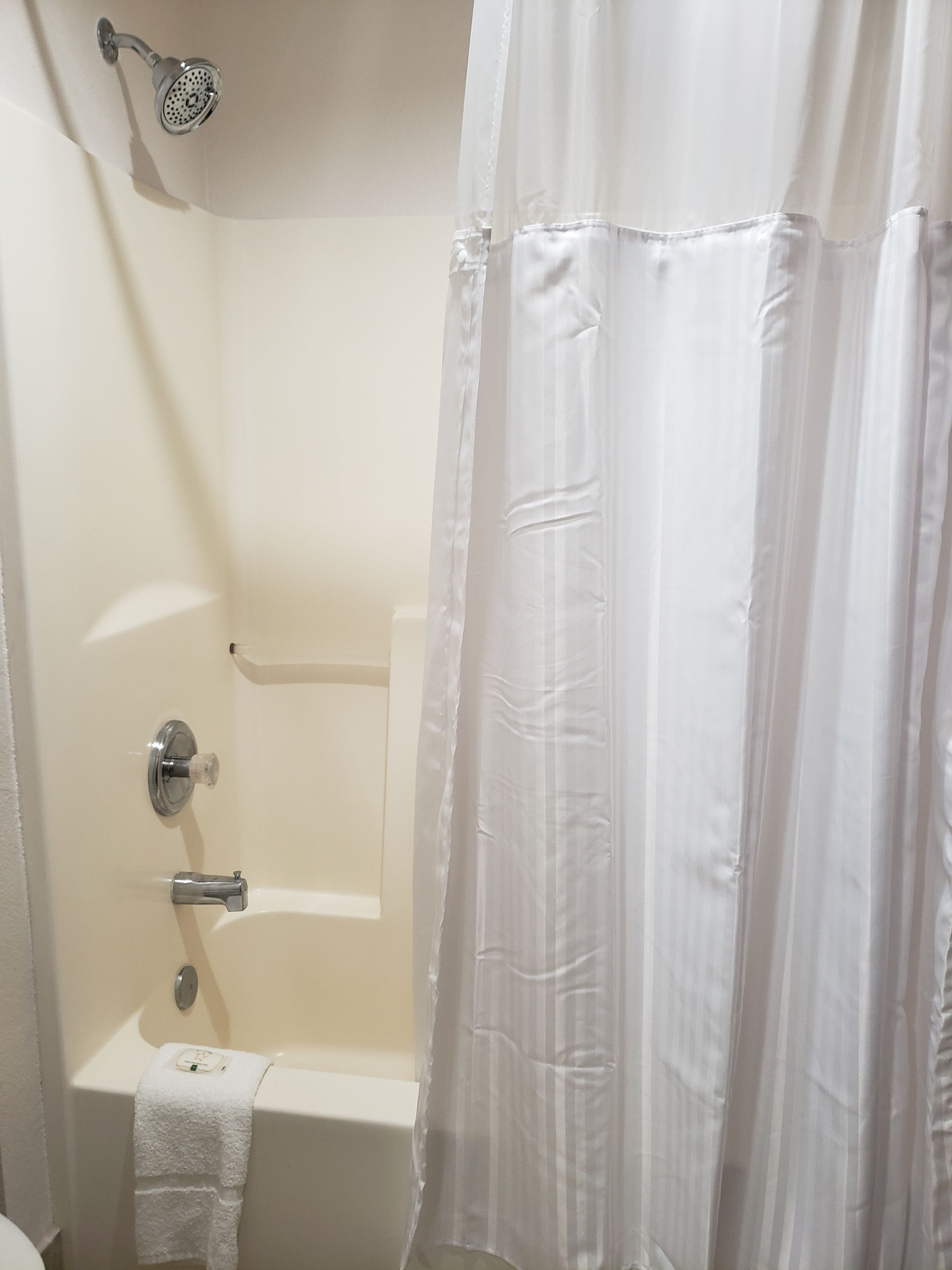 A bathroom with a bathtub, a showerhead, and a white curtain.