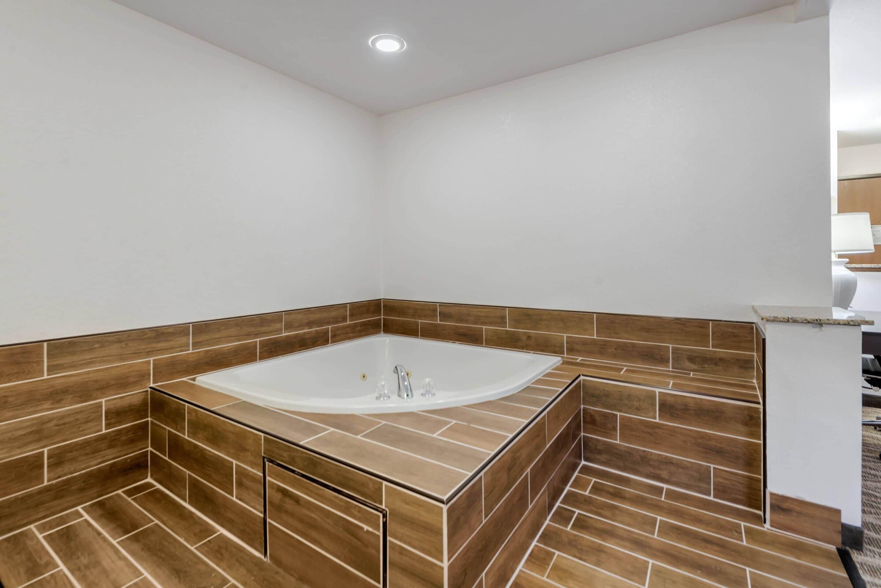 A modern bathroom with a freestanding bathtub, wooden floor tiles, and a white wall.