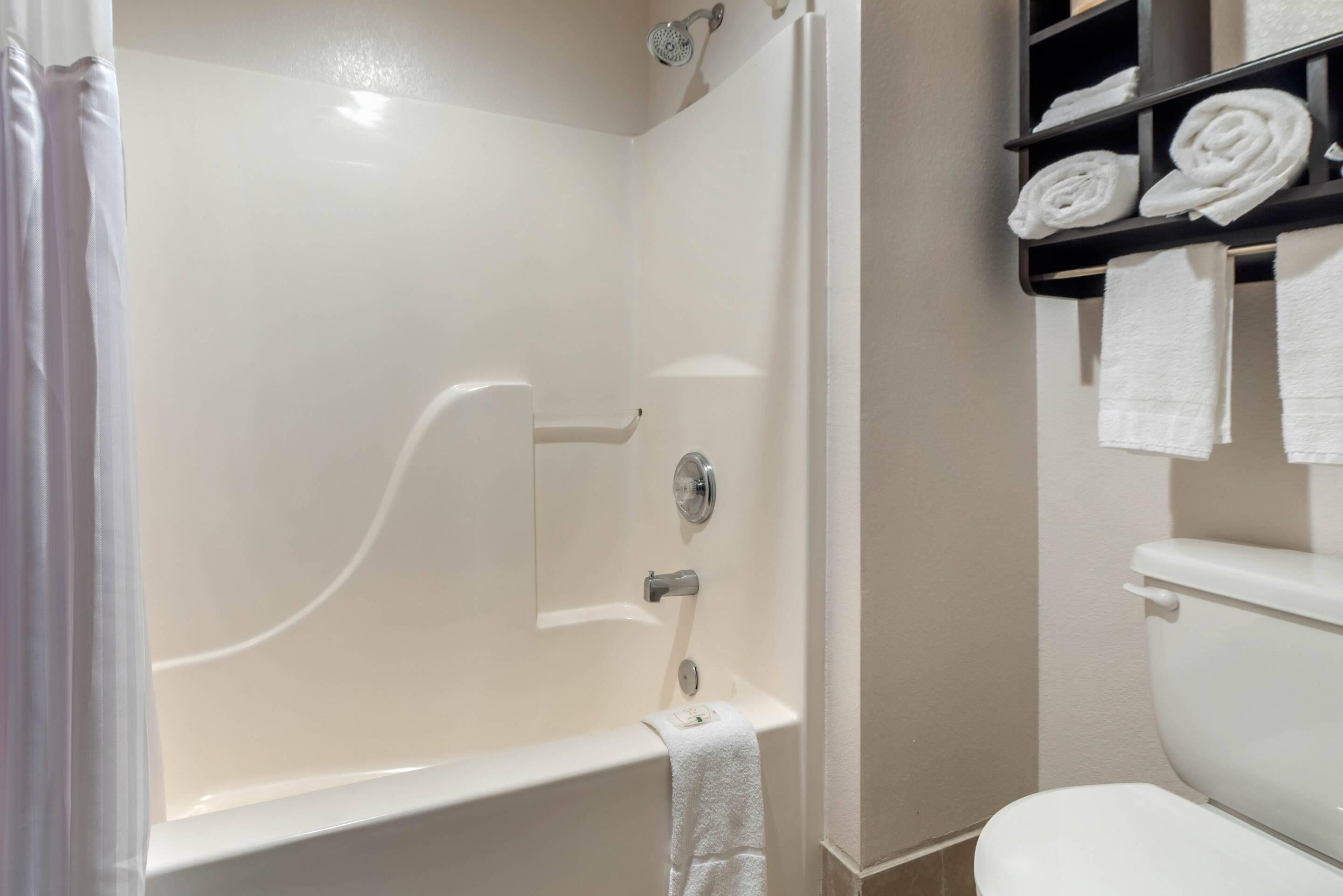 Un baño con bañera, inodoro y un estante con toallas enrolladas.