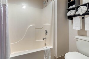 Un baño con bañera, inodoro y un estante con toallas enrolladas.
