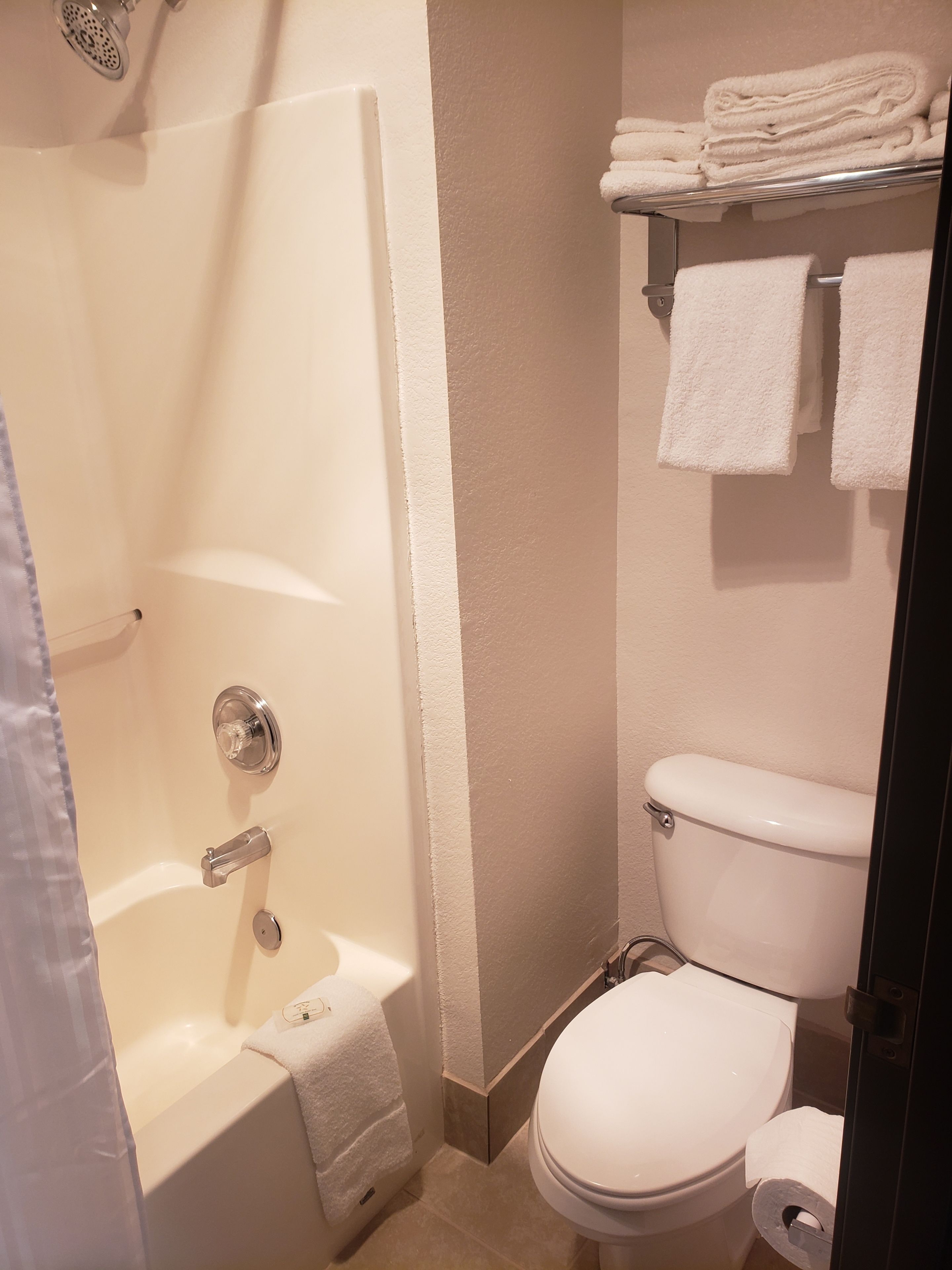 Une salle de bain avec une baignoire, des toilettes et une étagère où sont pliées des serviettes.