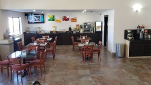 Un restaurante con varias mesas y sillas, una barra con máquina de café y un televisor montado en la pared.