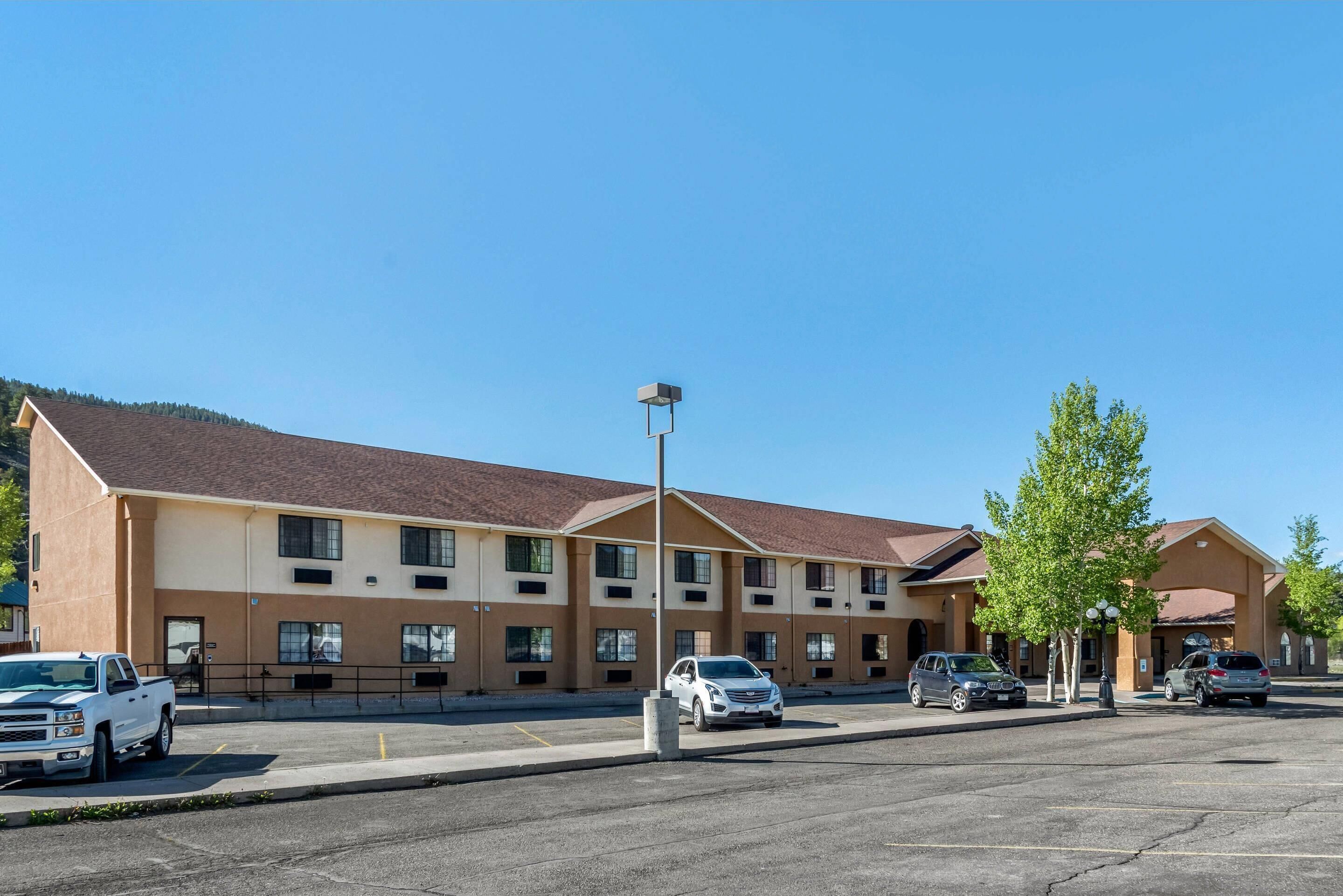 A multi-story hotel with a parking lot, a clear blue sky, and a mountain in the background.