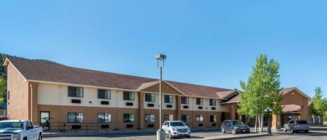 A multi-story hotel with a parking lot, a clear blue sky, and a mountain in the background.