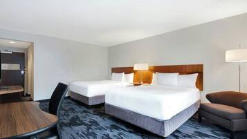 A hotel room with two beds, a desk, a chair, and a lamp.
