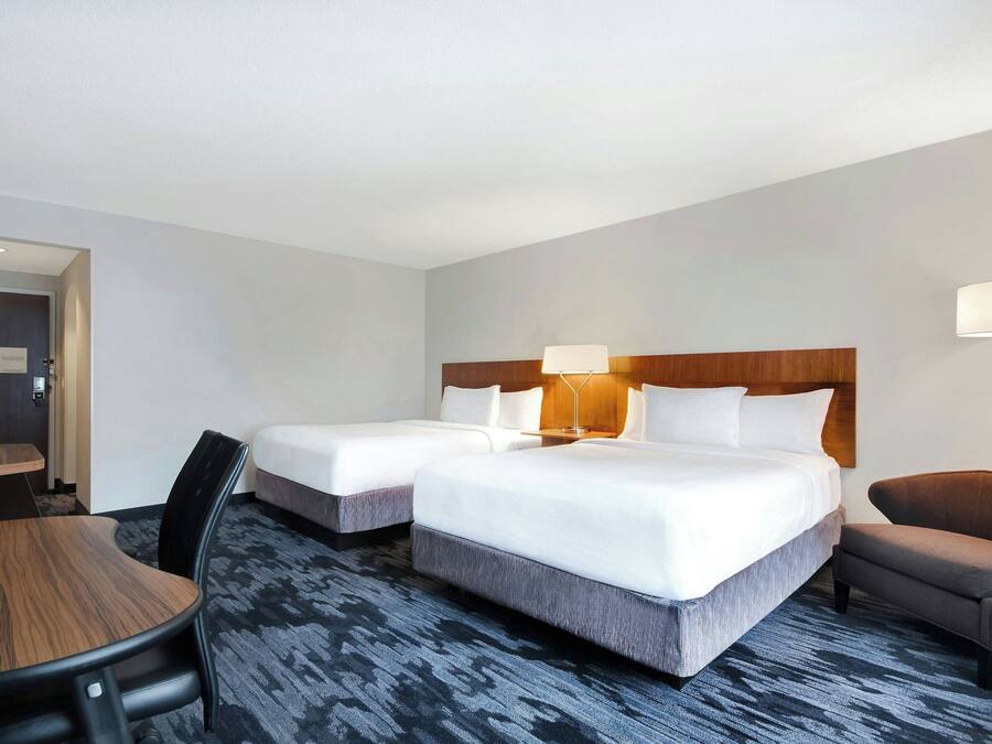 A hotel room with two beds, a desk, a chair, and a lamp.