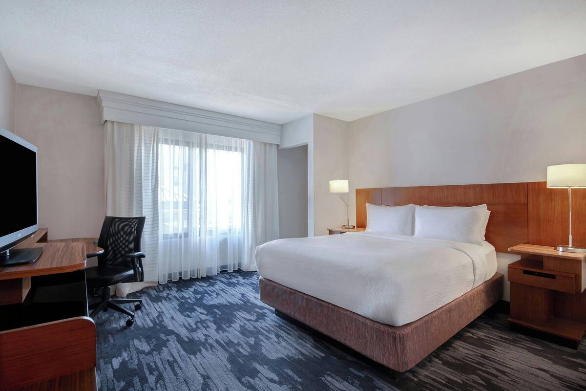 A hotel room with a large bed, a desk with a computer, a chair, and a TV.