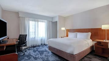 A hotel room with a large bed, a desk with a computer, a chair, and a TV.