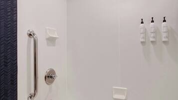 A modern bathroom with a white bathtub, a handheld showerhead, a handheld shower, and three bottles of shampoo on the wall.