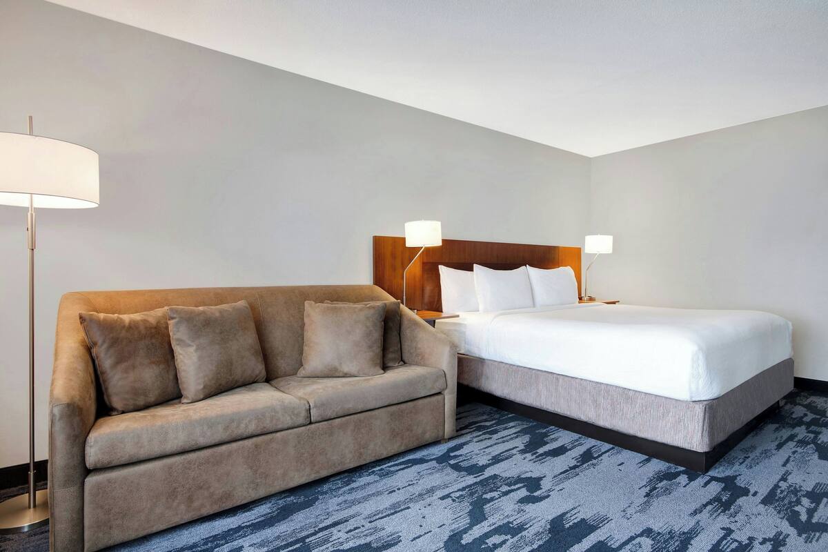 A hotel room with a bed, a sofa, and two bedside lamps.