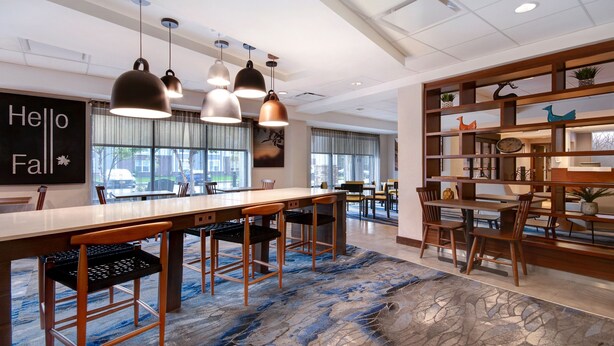 Un hall d’hôtel moderne avec un long comptoir d’accueil en bois, plusieurs espaces de détente et une bibliothèque décorative.