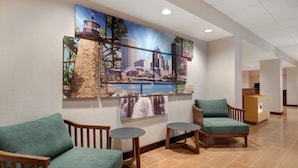 Un hall d’entrée agrémenté d’une grande fresque représentant un paysage urbain, deux fauteuils verts, une petite table ronde et un comptoir d’accueil.